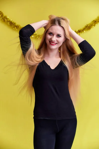 Conceito de uma jovem loira com decoração de Ano Novo. Retrato de uma menina bonita em uma camiseta preta com cabelo longo e bonito e ótima maquiagem. Sorrindo, mostrando emoções em um fundo amarelo . — Fotografia de Stock