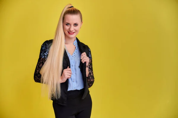 Retrato de uma mulher gerente em um terno de negócios com cabelo longo e bonito e excelente maquiagem em um fundo amarelo. Conceito de negócios menina loira fica na frente da câmera . — Fotografia de Stock