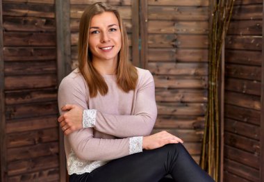 Çatı katı tarzı konsept. Evin içinde, ahşap bir arka planda pembe kazaklı güzel sarışın bir kızın portresi. Sevimli bakışlar ve kameraya gülümsemeler, düz bir sandalyede oturuyor.