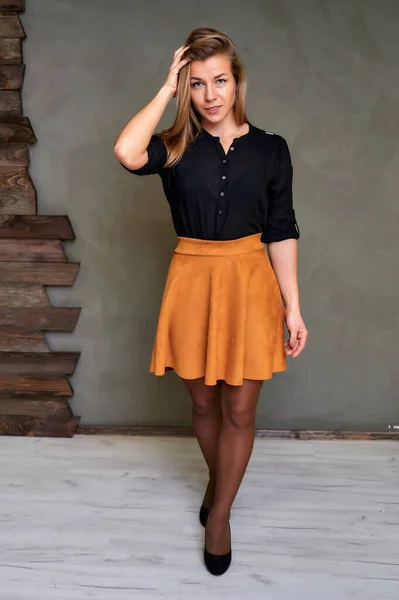 Полнометражный портрет симпатичной блондинки в черном свитере и оранжевой юбке на альтернативном фоне в винтажном интерьере. Симпатично смотрит в камеру, стоя прямо . — стоковое фото