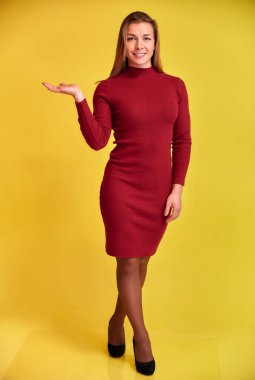 Sarı arka planda bordo bir elbise içinde güzel bir gülümsemesi olan hoş, formda, sarışın bir kızın tam boy dikey portresi. Kameraya bakıyor, dik duruyor..