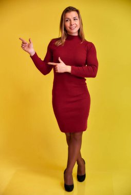 Sarı arka planda bordo bir elbise içinde güzel bir gülümsemesi olan hoş, formda, sarışın bir kızın tam boy dikey portresi. Kameraya bakıyor, dik duruyor..