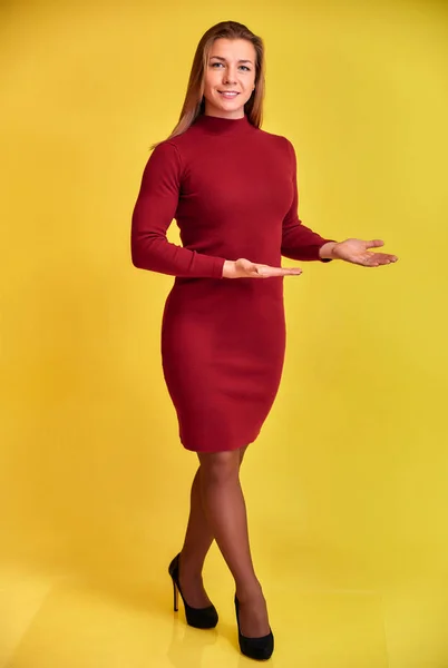 Retrato vertical de comprimento total de uma linda garota loira fitness com um belo sorriso em um vestido de Borgonha em um fundo amarelo. Bonito olha para a câmera, em pé em linha reta . — Fotografia de Stock