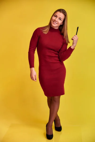 Retrato vertical de comprimento total de uma linda garota loira fitness com um belo sorriso em um vestido de Borgonha em um fundo amarelo. Bonito olha para a câmera, em pé em linha reta . — Fotografia de Stock