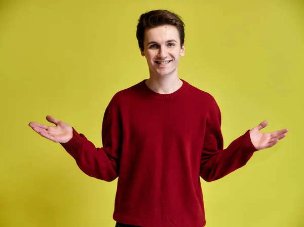 Retrato de um jovem bonito com um corte de cabelo curto e um sorriso largo em uma camisola borgonha em um fundo amarelo. Bonito olha para a câmera, em pé em linha reta . — Fotografia de Stock