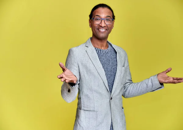 Porträtt av en ung afroamerikansk man med kort hår och ett vitt-tandat leende i en grå jacka på en gul bakgrund. Stå och prata framför kameran. — Stockfoto