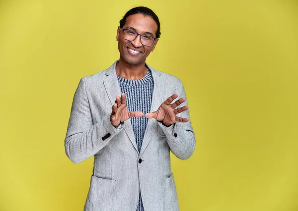 Retrato de un joven afroamericano con el pelo corto y una sonrisa de dientes blancos con una chaqueta gris sobre un fondo amarillo. De pie y hablando delante de la cámara . —  Fotos de Stock