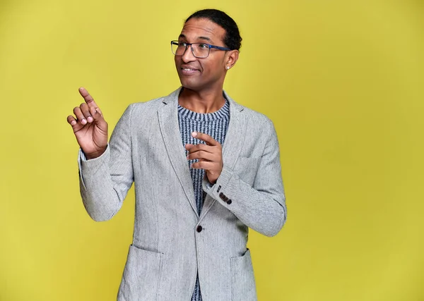 Porträtt av en ung afroamerikansk man med kort hår och ett vitt-tandat leende i en grå jacka på en gul bakgrund. Stå och prata framför kameran. — Stockfoto