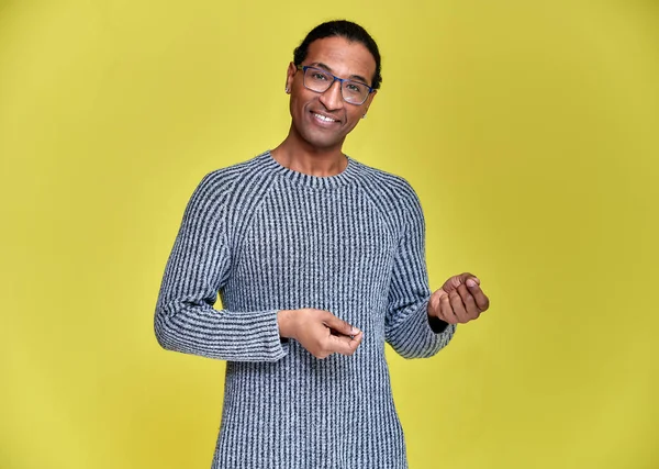 Porträtt av en ung afroamerikansk man i glasögon med en kort frisyr och med ett vitt-tandat leende i en grå tröja på en gul bakgrund. Stå och prata framför kameran. — Stockfoto