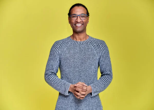 Retrato de un joven afroamericano en gafas con un corte de pelo corto y con una sonrisa de dientes blancos en un suéter gris sobre un fondo amarillo. De pie y hablando delante de la cámara . —  Fotos de Stock