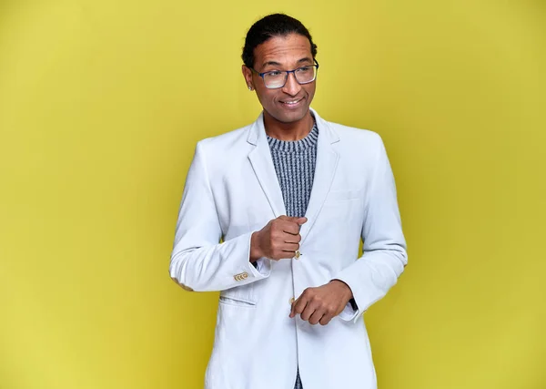 Retrato de un joven afroamericano con cortes de pelo cortos y una sonrisa de dientes blancos con una chaqueta blanca sobre un fondo amarillo. De pie y hablando delante de la cámara . —  Fotos de Stock