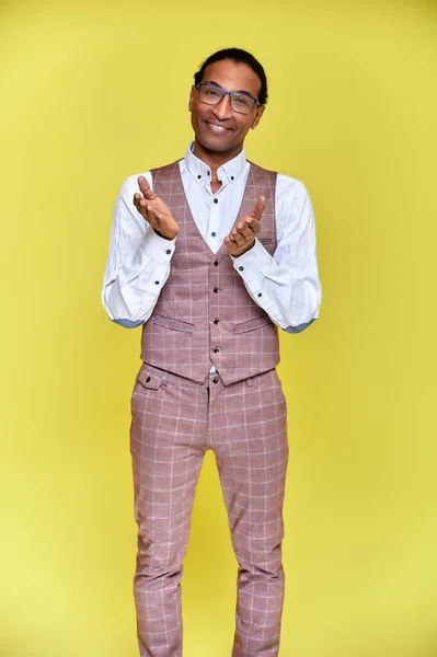 Vertikalt porträtt Ung man med kort hår afroamerikan i en kostym på en gul bakgrund. Stå och prata framför kameran. — Stockfoto