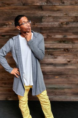 Dikey Portre Genç adam, kısa saçlı, Afro-Amerikan gözlüklü, sıradan giyimli, klasik ahşap arka planda, bir çatı katı tarzında bir evin içinde. Kameranın önünde dikiliyorum.