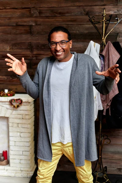 Retrato vertical Hombre joven con gafas afroamericanas de pelo corto en ropa ordinaria sobre un fondo de madera vintage en el interior de una casa en un estilo loft. De pie justo delante de la cámara — Foto de Stock