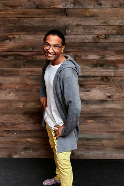 Vertikalt porträtt Ung man med kort hår afroamerikanska glasögon i vanliga kläder på en vintage trä bakgrund i ett hem inredning i en loft stil. Stående framför kameran — Stockfoto