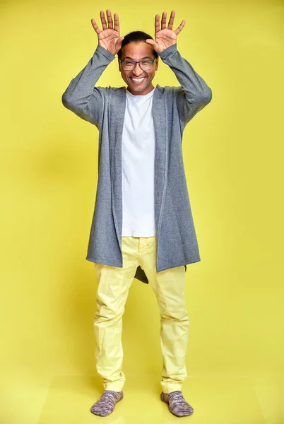 Vertical portrait of a cheerful young man wearing glasses African-American with a short haircut in ordinary clothes on a yellow background in full length. Standing right in front of the camera — Stock Photo, Image