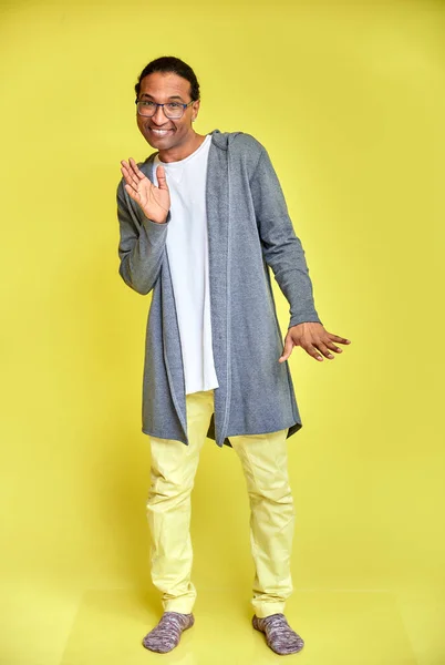 Vertical portrait of a cheerful young man wearing glasses African-American with a short haircut in ordinary clothes on a yellow background in full length. Standing right in front of the camera — Stock Photo, Image
