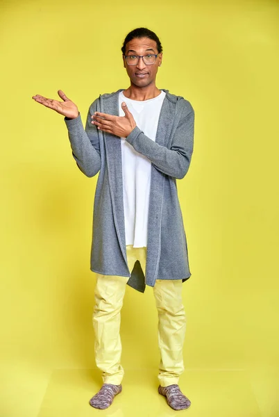 Retrato vertical de un joven alegre con gafas afroamericanas con un corte de pelo corto en ropa ordinaria sobre un fondo amarillo en toda su longitud. De pie justo delante de la cámara —  Fotos de Stock