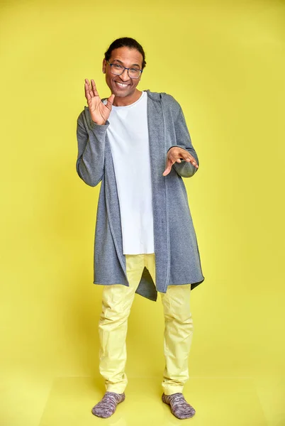 Retrato vertical de un joven alegre con gafas afroamericanas con un corte de pelo corto en ropa ordinaria sobre un fondo amarillo en toda su longitud. De pie justo delante de la cámara —  Fotos de Stock