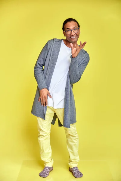 Das vertikale Porträt eines fröhlichen jungen Mannes mit Brille afrikanisch-amerikanisch mit Kurzhaarschnitt in gewöhnlicher Kleidung auf gelbem Hintergrund in voller Länge. direkt vor der Kamera stehen — Stockfoto