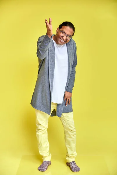 Retrato vertical de un joven alegre con gafas afroamericanas con un corte de pelo corto en ropa ordinaria sobre un fondo amarillo en toda su longitud. De pie justo delante de la cámara —  Fotos de Stock