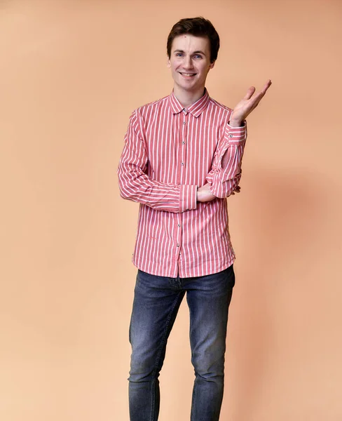 Retrato vertical de um jovem caucasiano com cabelo curto e um sorriso de dentes brancos em uma camisa rosa em um fundo rosa. De pé e falando bem na frente da câmera mostrando as mãos . — Fotografia de Stock