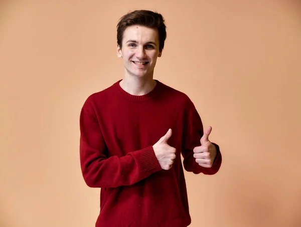 Retrato de un joven caucásico con el pelo corto y una sonrisa de dientes blancos en un suéter de color burdeos sobre un fondo rosa. De pie y hablando justo delante de la cámara mostrando las manos . — Foto de Stock