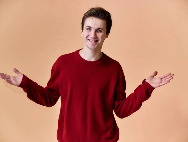 Portrait of a young Caucasian man with short hair and a white-toothed smile in a burgundy sweater on a pink background. Standing and talking right in front of the camera showing hands.