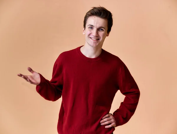 Portrét mladého bělocha s krátkými vlasy a bílým úsměvem v purpurovém svetru na růžovém pozadí. Stojící a mluvící přímo před kamerou ukazující ruce. — Stock fotografie