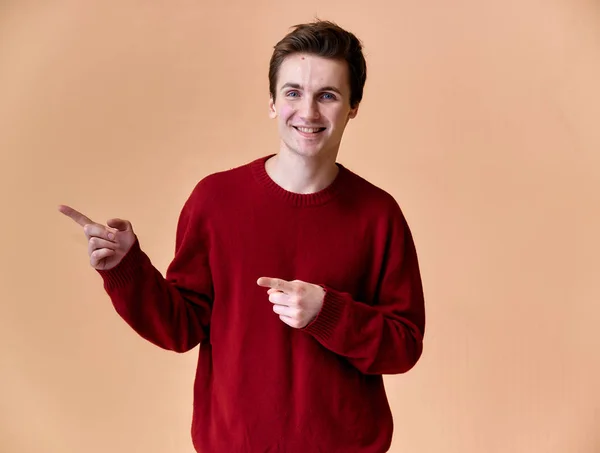 Retrato de un joven caucásico con el pelo corto y una sonrisa de dientes blancos en un suéter de color burdeos sobre un fondo rosa. De pie y hablando justo delante de la cámara mostrando las manos . — Foto de Stock