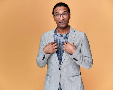 Kısa saçlı, beyaz dişli, pembe arka planda gri ceketli genç bir Afrikalı Amerikalı 'nın portresi. Kameranın önünde dikilip konuşmak..