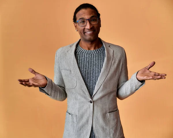 Portrett av en ung afroamerikansk mann med kort hår og et hvitt smil i grå jakke på rosa bakgrunn. Står og snakker rett foran kamera . – stockfoto