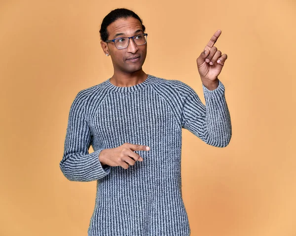 Retrato de un joven afroamericano en gafas con un corte de pelo corto y con una sonrisa de dientes blancos en un suéter gris sobre un fondo rosa. De pie y hablando delante de la cámara . —  Fotos de Stock