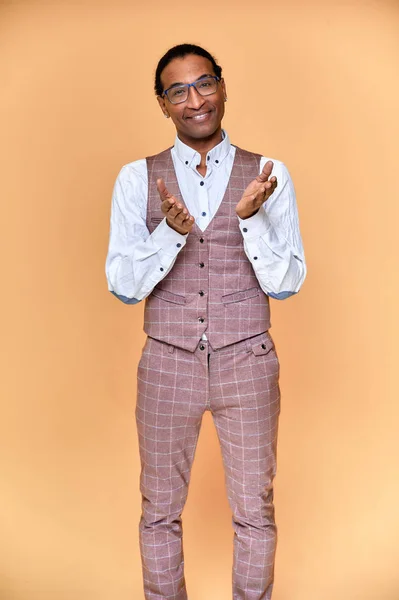Retrato vertical Joven con afroamericano de pelo corto en un traje de negocios sobre un fondo rosa. De pie y hablando delante de la cámara . —  Fotos de Stock