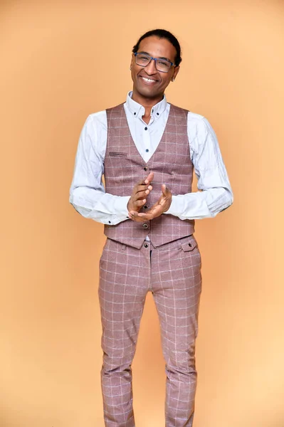 Vertikalt porträtt Ung man med kort hår afroamerikan i en kostym på en rosa bakgrund. Stå och prata framför kameran. — Stockfoto