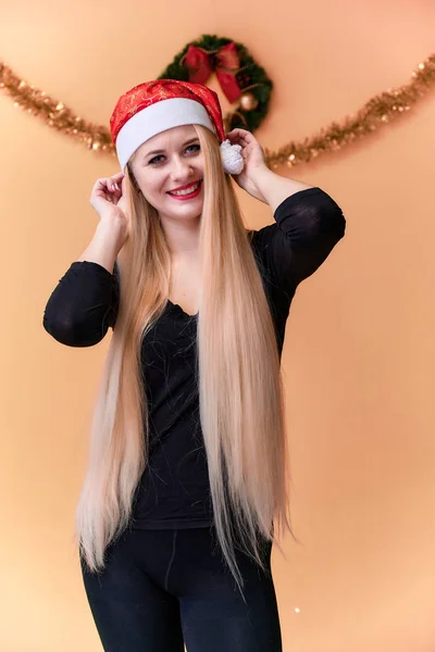 Retrato de una linda chica en una camiseta negra con pelo largo y hermoso y gran maquillaje. Concepto de una joven rubia con decoración de Año Nuevo. Sonriendo, mostrando emociones sobre un fondo rosado . —  Fotos de Stock