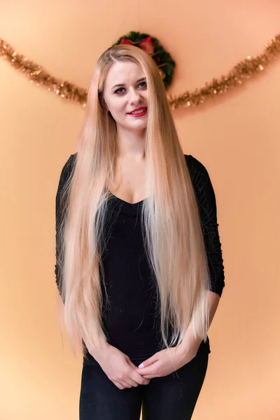 Retrato de uma menina bonita em uma camiseta preta com cabelo longo e bonito e ótima maquiagem. Conceito de uma jovem loira com decoração de Ano Novo. Sorrindo, mostrando emoções em um fundo rosa . — Fotografia de Stock