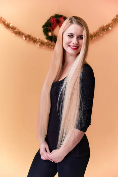 Portret uroczej dziewczyny w czarnej koszulce z długimi, pięknymi włosami i świetnym makijażem. Koncepcja młodej blondynki z noworocznym wystrojem. Uśmiechnięta, pokazująca emocje na różowym tle. — Zdjęcie stockowe