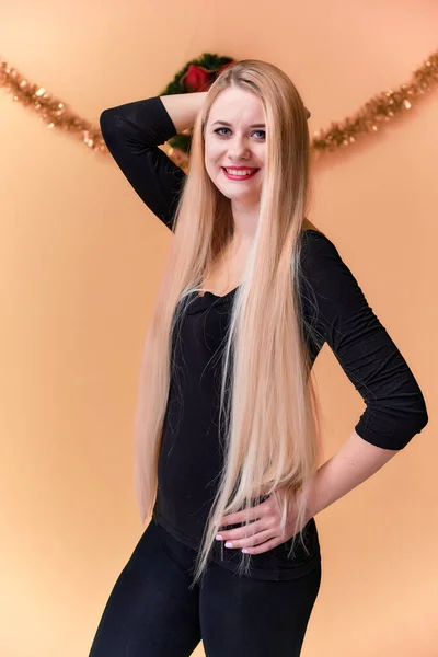 Retrato de una linda chica en una camiseta negra con pelo largo y hermoso y gran maquillaje. Concepto de una joven rubia con decoración de Año Nuevo. Sonriendo, mostrando emociones sobre un fondo rosado . — Foto de Stock