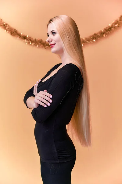 Retrato de una linda chica en una camiseta negra con pelo largo y hermoso y gran maquillaje. Concepto de una joven rubia con decoración de Año Nuevo. Sonriendo, mostrando emociones sobre un fondo rosado . —  Fotos de Stock