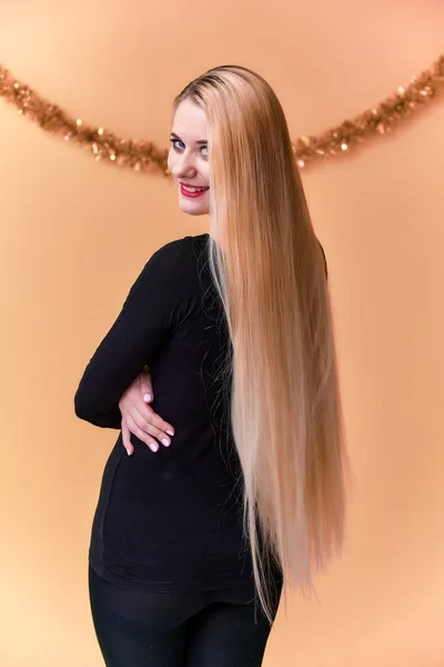 Porträt eines süßen Mädchens in einem schwarzen T-Shirt mit langen, schönen Haaren und tollem Make-up. Konzept einer jungen blonden Frau mit Weihnachtsdekor, Rückansicht. Lächeln auf rosa Hintergrund. — Stockfoto