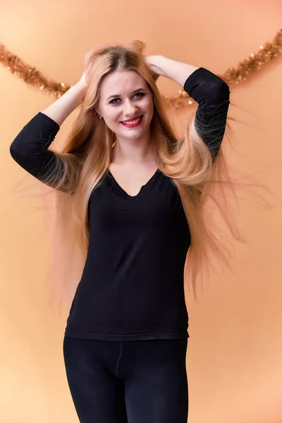 Retrato de una linda chica en una camiseta negra con pelo largo y hermoso y gran maquillaje. Concepto de una joven rubia con decoración de Año Nuevo. Sonriendo, mostrando emociones sobre un fondo rosado . —  Fotos de Stock