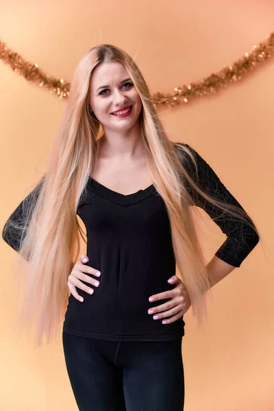 Portret uroczej dziewczyny w czarnej koszulce z długimi, pięknymi włosami i świetnym makijażem. Koncepcja młodej blondynki z noworocznym wystrojem. Uśmiechnięta, pokazująca emocje na różowym tle. — Zdjęcie stockowe