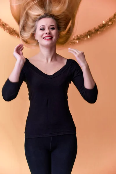 Portret van een schattig meisje in een zwart T-shirt met lang mooi haar en geweldige make-up. Concept van een jonge blonde vrouw met nieuwjaarsdecor. Lachen, emoties tonen op een roze achtergrond. — Stockfoto
