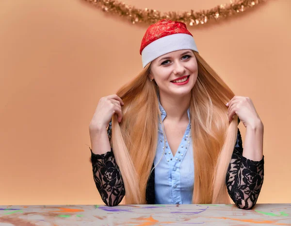 Porträt einer Frau im Businessanzug mit langen, schönen Haaren und exzellentem Make-up mit Neujahrsdekor auf rosa Hintergrund. das Konzept der Neujahrsstimmung eines blonden Mädchens sitzt an einem Tisch. — Stockfoto