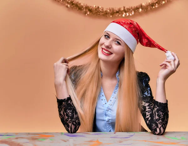 Porträt einer Frau im Businessanzug mit langen, schönen Haaren und exzellentem Make-up mit Neujahrsdekor auf rosa Hintergrund. das Konzept der Neujahrsstimmung eines blonden Mädchens sitzt an einem Tisch. — Stockfoto