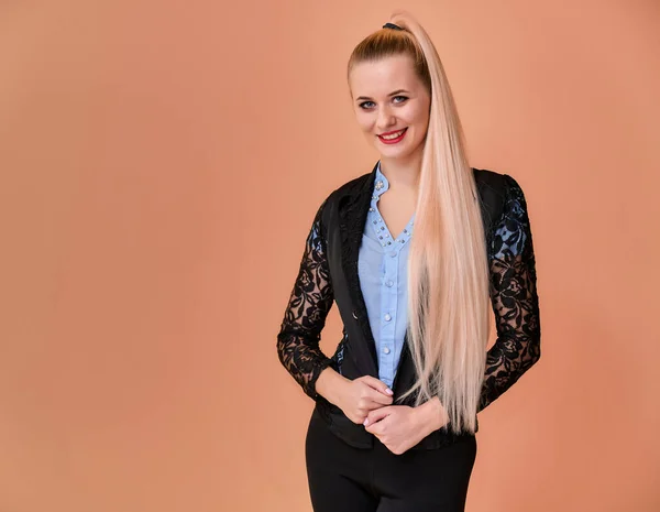 Concept business blonde meisje staat voor de camera. Portret van een manager vrouw in een zakenpak met lang mooi haar en uitstekende make-up op een roze achtergrond. — Stockfoto