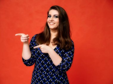 Güzel bir esmer kadın portresi, güzel bir saç stili ve koyu mavi bir bluz ve kırmızı bir arka planı var. Gülümseyerek duruyor ve ellerini duygularıyla gösteriyor..