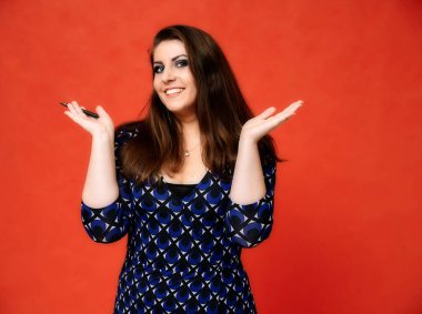 Güzel bir esmer kadın portresi, güzel bir saç stili ve koyu mavi bir bluz ve kırmızı bir arka planı var. Gülümseyerek duruyor ve ellerini duygularıyla gösteriyor..