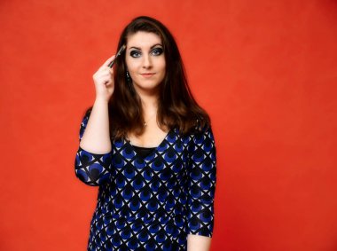 Güzel bir esmer kadın portresi, güzel bir saç stili ve koyu mavi bir bluz ve kırmızı bir arka planı var. Gülümseyerek duruyor ve ellerini duygularıyla gösteriyor..